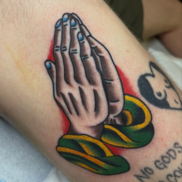 Traditional praying hands tattoo with green and gold cuffs