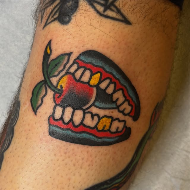 Traditional chattering teeth tattoo biting a red cherry
